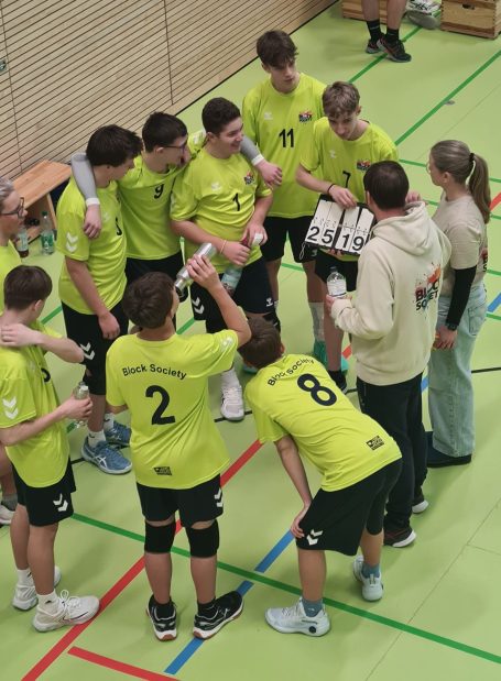Unsere Jugend Junge Volleyballmannschaft in grünen Trikots bespricht Taktiken in einer Sporthalle.